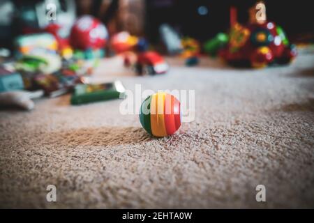 Shallow depth of field (selective focus) image with a colored rubber ball on the floor of a toddler’s room, with toys in the background. Stock Photo