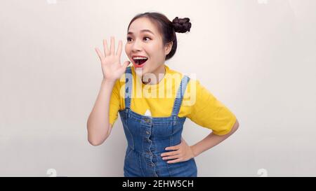 Asian happy portrait beautiful young woman standing smiling profile shouting and holding hand near her open mouth on white background Stock Photo