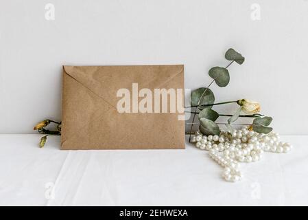 Fashionable stock stationery background-kraft envelope and dried plants and flowers on a white table.Romantic feminine background. Blank for an invita Stock Photo