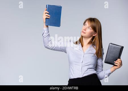 Caucasian young woman in gray shirt holding up two books. Portrait of smiling businesswoman, teacher or university student, isolated on gray Stock Photo