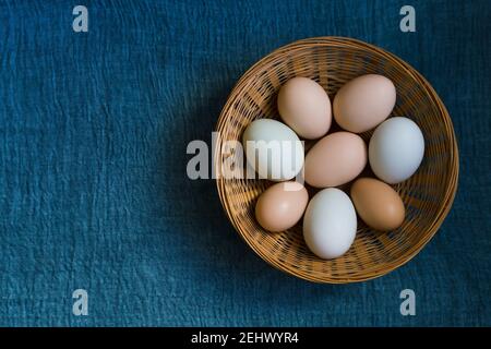Organic chicken eggs in wicker basket on blue textile background with copy space Stock Photo