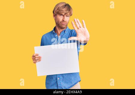Handsome caucasian man with beard holding sale poster with open hand doing stop sign with serious and confident expression, defense gesture Stock Photo