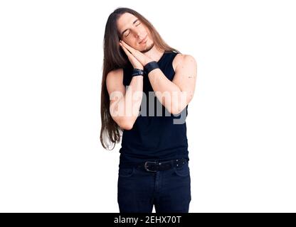 Young adult man with long hair wearing goth style with black clothes sleeping tired dreaming and posing with hands together while smiling with closed Stock Photo