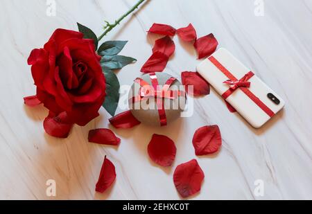 smart and mobile speaker wrapped with red bow with rose and rose petals on white marble background Stock Photo
