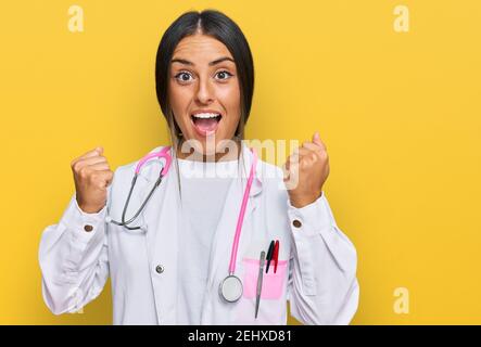 Beautiful hispanic woman wearing doctor uniform and stethoscope celebrating surprised and amazed for success with arms raised and open eyes. winner co Stock Photo