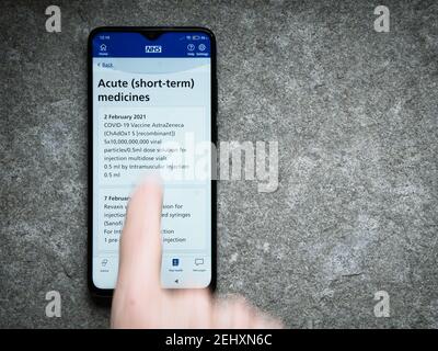 The UK's NHS smartphone app shows evidence of an Oxford  AstraZeneca COVID vaccination given given on 2nd February 2021. A blurred finger is swiping d Stock Photo