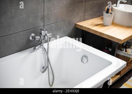 Bathroom interior with grey tile on a wall, stylish white bath with a silver tap. Minimalism in interior of bathroom. Stock Photo