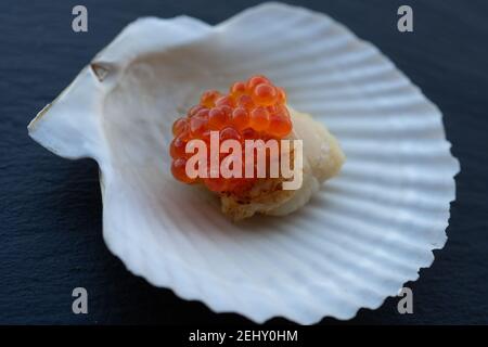 Scallop on a shell with a cap of red caviar. Seafood delicacy. Stock Photo
