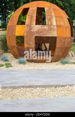 A corten steel rusted steel pod structure with a gravel bed garden planted with grasses and large giant stone paving slabs England GB UK Stock Photo