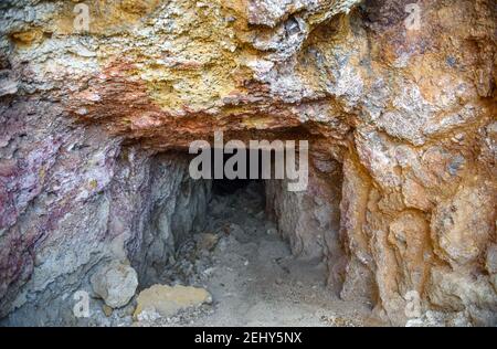 Dark tunnel of the abandoned mine with colorful rocks at the entrance rich with copper ore and sulfides Stock Photo