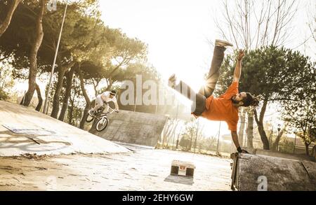Urban athlete breakdancer performing acrobatic jump flip at skate park - Guy riding bmx bicycle behind mate acrobat dancing with extreme move Stock Photo