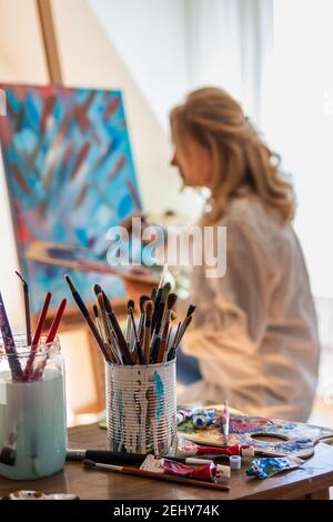 Art painter working on her abstract paintings at workshop. Selective focus on paintbrushes, palette and colors. Woman in art studio Stock Photo