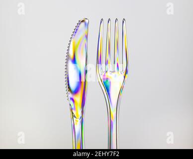 Transparent plastic fork and knife, rainbow colored by photoelasticity isolated on light gray background. Stock Photo