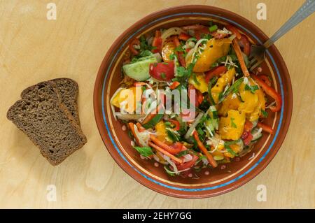 Top view on bowl with vegan salad standing on wooden table next two slices of brown bread Stock Photo