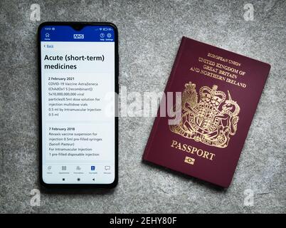 The UK's NHS smartphone app shows evidence of an Oxford AstraZeneca COVID vaccination given given on 2nd February 2021. A UK passport appears on the r Stock Photo