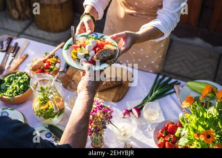 Catering service outdoors. Enjoy fresh caprese salad with mozzarella and baguette. Woman serving vegetarian food on plate to another person at garden Stock Photo