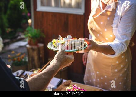 Woman serving vegetable salad with baguette on plate to another person at garden party. Catering service at celebration event outdoors Stock Photo