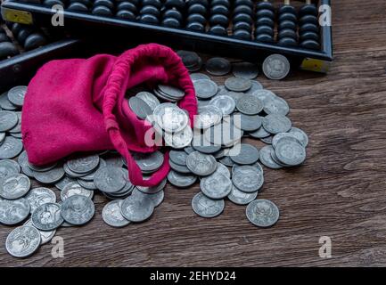 Vintage wooden hand abacus with pile of money coins from red cloth bag on rustic old wooden table. Concept for making business and saving money of chi Stock Photo