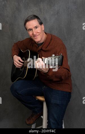 man sitting on stool picking acoustic guitar smiling at camera Stock Photo