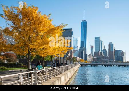 Lower Manhattan skyscraper stands behind the autumn leaf color trees along the Hudson River at New York City NY USA. Stock Photo