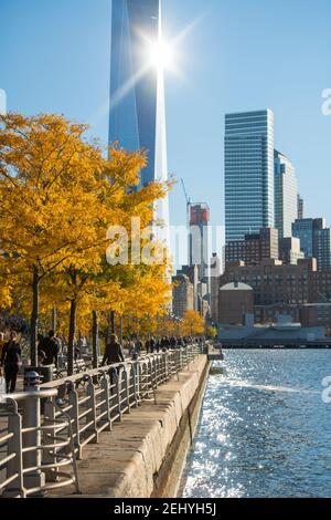 Lower Manhattan skyscraper stands behind the autumn leaf color trees along the Hudson River at New York City NY USA. Stock Photo