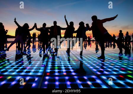 Zadars Greeting to the Sun Lightshow Installation with Silhouettes of People Dancing on it and Sunset in the Background Stock Photo