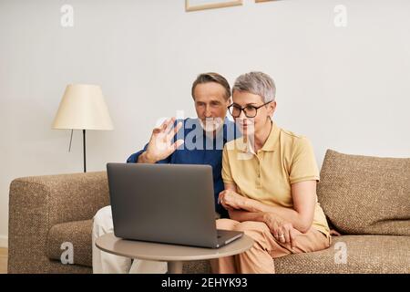 Senior couple using a laptop for video call. Mature man greeting with a hand wave Stock Photo