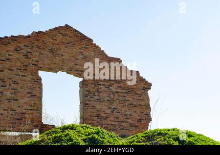 The wall of the building with doorway is a front view with pile of red brick debris and construction debris against the blue sky and green hills. Back Stock Photo