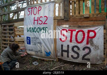 Aylesbury, Buckinghamshire, UK. 20th February, 2021. A protester fastens a Stop HS2 banner outside the new protest camp. HS2 Ltd took over a wood called the Spinney earlier this week and have started to destroy it. Stop HS2 activists have set up a new camp in the woodlands near it in an attempt to stop HS2 from felling the trees. The number of protesters is growing by the day as people get to see just how destructive the High Speed Rail from London to Birmingham is to the environment. Credit: Maureen McLean/Alamy Live News Stock Photo