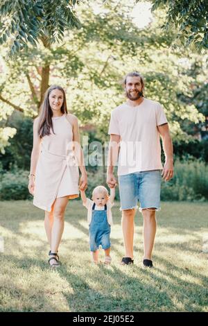 Happy smiling mother and father hold hands with baby boy in park outdoor. Family Caucasian mom and dad with son walking together. Happy family Stock Photo