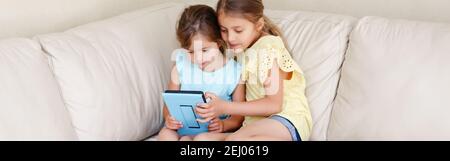 Two Caucasian girls sisters watching playing on digital tablet. Kids using digital gadget. Candid authentic lifestyle early development. New technolog Stock Photo