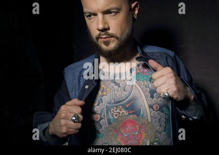 Young handsome masculin man , in unfastened denim jacket with japanese tattoos on his chest. Stock Photo