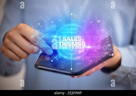 Businessman holding a foldable smartphone with SALES TRAINING inscription, new business concept