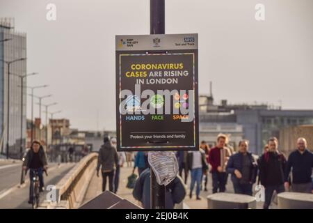 People walk past a 'Coronavirus Cases Are Rising In London' sign on London Bridge during the coronavirus lockdown. London, United Kingdom, February 2021. Stock Photo