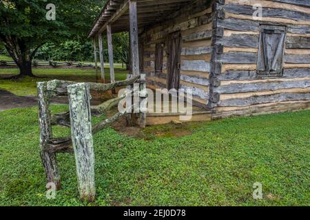 Abandoned old pioneer log cabin closeup view of the front entry with porch locked and boarded up surrounded by a rustic wooden fence and trees in the Stock Photo
