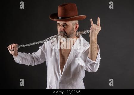 A bearded short-haired elderly man with a metal chain in his hands shows a rockers goat Stock Photo