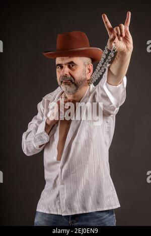 A bearded short-haired elderly man with a metal chain in his hands shows a rockers goat Stock Photo