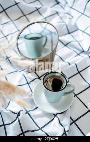 Morning cozy mood. Coffee in the bed. A cup of black coffee in bed on white checkered blanket Stock Photo