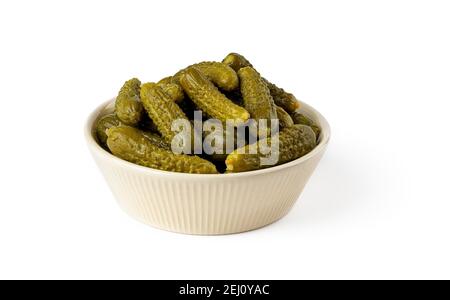 Pickled gherkins in a beige ceramic bowl isolated on a white background. Whole green cornichons marinated with dill, garlic and mustard seeds. Stock Photo