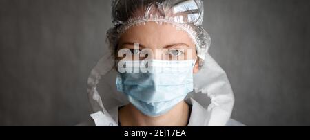 Woman wearing protective glasses and medical face mask due to COVID-19 coronavirus pandemic, panoramic banner with portrait of female doctor or nurse Stock Photo