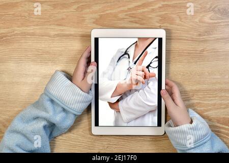 Remote online telemedicine. A child in home clothes with a tablet in his hands. On the screen video consultation with the doctor. Recommendations for treatment. Stock Photo