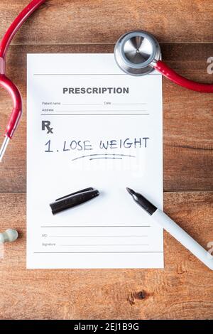Close up flat lay image of a doctor's office desk with a stethoscope, pen and a prescription that has one item 'Lose weight' prescribed. A concept ima Stock Photo