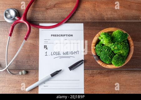 Close up flat lay image of a doctor's office desk with a bowl of broccoli,  stethoscope, pen and a prescription that has one item 'Lose weight' prescr Stock Photo