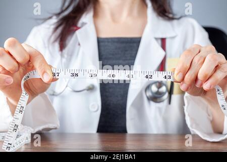 Close up isolated image of a caucasian doctor holding a tape measure in her hands which shows 40 inches as abdominal circumference upper limit in heal Stock Photo