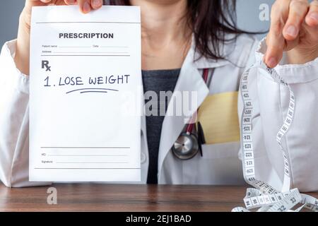 A female physician is holding a prescription that says lose weight in one hand and a tape measure for abdominal circumference measurement on the other Stock Photo