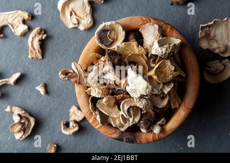 Close up isolated flat lay image of a rustic wooden bowl filled with sliced and dried mushroom pieces. The bowl is on dark stone surface. There is an Stock Photo