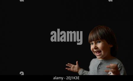 Portrait of amazed cute little kid pointing to empty place on background, surprised preschooler showing copy space for promotional ad. indoor studio s Stock Photo