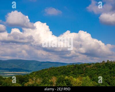 Massive clouds - towering cumulus - forming in the blue sky over hilly landscape. Stock Photo