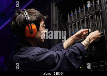 Side view portrait of tattooed young network engineer setting up servers in supercomputer data center, copy space Stock Photo