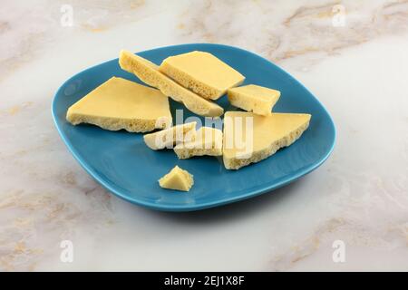 Broken caramel bubble white chocolate bar pieces on blue snack plate on table Stock Photo